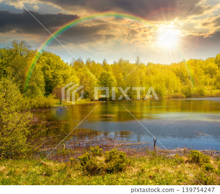 sunset over landscape by the lake. deciduous forest near the glacial lake. view of primeval forest of carpathian mountains in spring. cloudy sky. hiking and tourism background. weather with rainbow 139754247