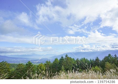 A landscape of forests enveloped in blue sky and clouds, with distant mountains in the background. A landscape of forests enveloped in blue sky and clouds, with distant mountains in the background. 139754286