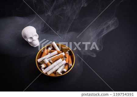 Smoking danger concept with skull cigarette butts and dark smoke background Smoking danger concept with skull cigarette butts and dark smoke background 139754391