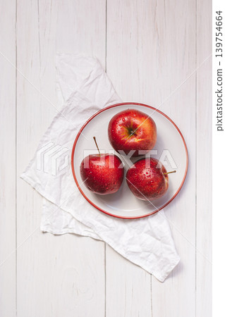 Three ripe red apples on a white plate. Top view on wooden table with a napkin. 139754664
