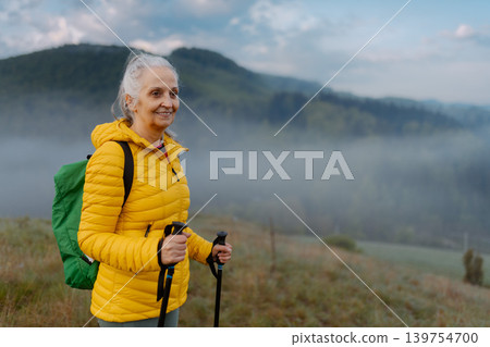 Senior woman hiking in nature on early morning with fog and mountains in background. Senior woman hiking in nature on early morning with fog and mountains in background. 139754700