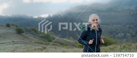 Senior woman hiking in nature on early morning with fog and mountains in background. 139754710