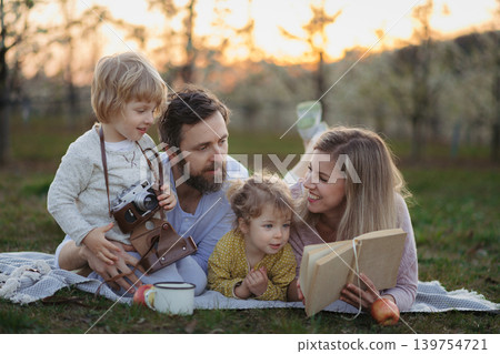 Family having picnic in spring nature, reading book on picnic blanket. 139754721