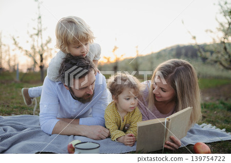 Family having picnic in spring nature, reading book on picnic blanket. Family having picnic in spring nature, reading book on picnic blanket. 139754722