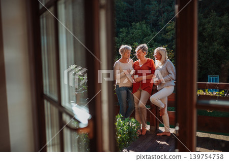 Senior female friends enjoying coffee together on cabin terrace getaway. 139754758