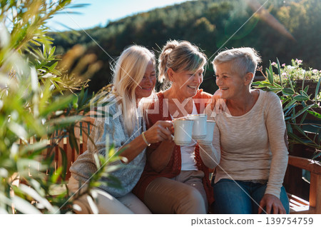 Senior female friends enjoying coffee together on cabin terrace getaway. 139754759