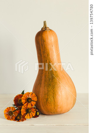 Ripe orange pumpkin on a pastel beige background with flowers of Helenium autumnale. Thanksgiving card or background. Ripe orange pumpkin on a pastel beige background with flowers of Helenium autumnale. Thanksgiving card or background. 139754780