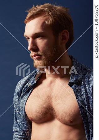 Fashion, thinking or model with chest in studio on a blue background wearing an open unbuttoned shirt. Ginger, body or handsome male person posing on color wall for masculine style, health or fitness Fashion, thinking or model with chest in studio on a blue background wearing an open unbuttoned shirt. Ginger, body or handsome male person posing on color wall for masculine style, health or fitness 139755270