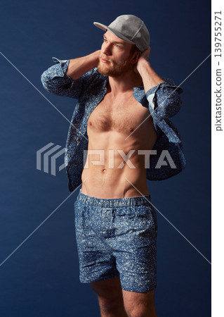 Fashion, body or model with six pack in studio on a blue background in an open unbuttoned shirt. Thinking, chest or handsome male person posing on color wall for masculine style with a trendy cap Fashion, body or model with six pack in studio on a blue background in an open unbuttoned shirt. Thinking, chest or handsome male person posing on color wall for masculine style with a trendy cap 139755271