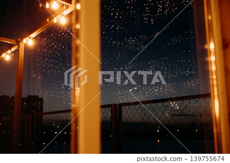 Cozy night rooftop atmosphere with hanging string lights and starry sky reflections. Warm glowing light bulbs against dark city skyline background. Magical evening terrace vibe and festive mood. Cozy night rooftop atmosphere with hanging string lights and starry sky reflections. Warm glowing light bulbs against dark city skyline background. Magical evening terrace vibe and festive mood. 139755674