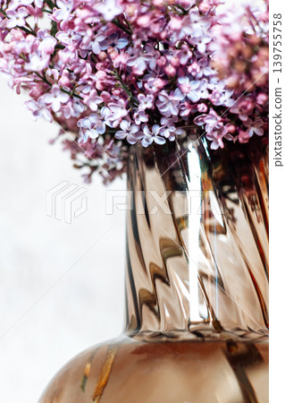 Close-up of blooming purple lilac flowers in elegant fluted glass vase. Beautiful floral textures, soft daylight, and spring botanical aesthetic for modern interior design and branding. Close-up of blooming purple lilac flowers in elegant fluted glass vase. Beautiful floral textures, soft daylight, and spring botanical aesthetic for modern interior design and branding. 139755758