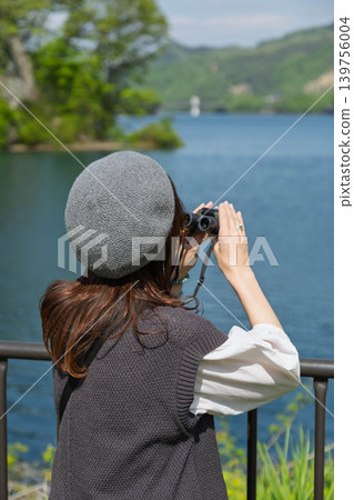 A woman looking through binoculars at a lake in early summer. A woman looking through binoculars at a lake in early summer. 139756004
