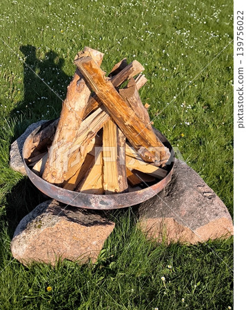 A fireplace made of stones and metal with neatly stacked firewood against a backdrop of green grass. A fireplace made of stones and metal with neatly stacked firewood against a backdrop of green grass. 139756022
