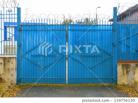 Weathered gate with rusted hinges. Industrial gate showing signs of decay and urban abandonment Weathered gate with rusted hinges. Industrial gate showing signs of decay and urban abandonment 139756130