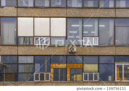 Rustic city building. Aged facade with glass reflections. Worn exterior featuring vents and reflective glass Rustic city building. Aged facade with glass reflections. Worn exterior featuring vents and reflective glass 139756131