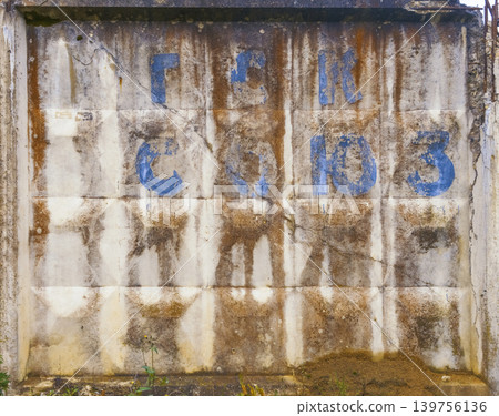 Urban weathered signage. Worn blue inscriptions on aged concrete with rust streaks and peeling paint 139756136