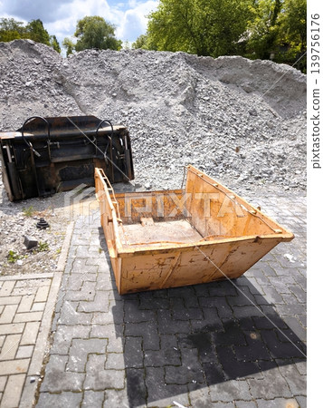 A construction container and an excavator bucket against a pile of crushed stone. A construction container and an excavator bucket against a pile of crushed stone. 139756176