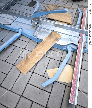 A blue manual tile cutter lies on paving slabs. Scraps of porcelain stoneware lie nearby. 139756177