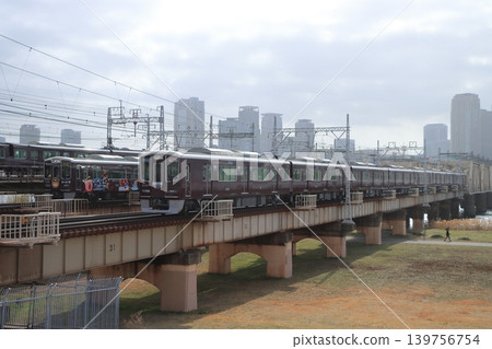 Hankyu trains cross the Shin-Yodogawa Bridge, with its tracks lined up against the backdrop of Osaka's urban landscape. 139756754