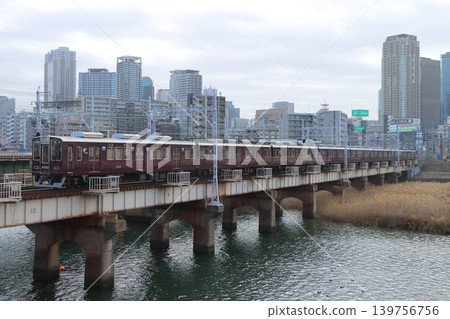 A Hankyu Kobe Line 8000 series train crosses the Shin-Yodogawa Bridge with a row of railway tracks and the Osaka cityscape in the background. (February 23, 2026) 139756756