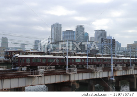 Hankyu trains cross the Shin-Yodogawa Bridge, with its tracks lined up against the backdrop of Osaka's urban landscape. 139756757