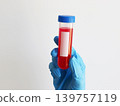 Gloved hand holding laboratory test tube with red liquid for virus testing and infectious disease diagnostics. Healthcare concept for medical research, sample analysis and pathogen detection. 139757119