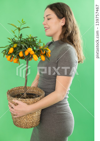 Young woman in gray dress with potted miniature kumquat in her hands Young woman in gray dress with potted miniature kumquat in her hands 139757467