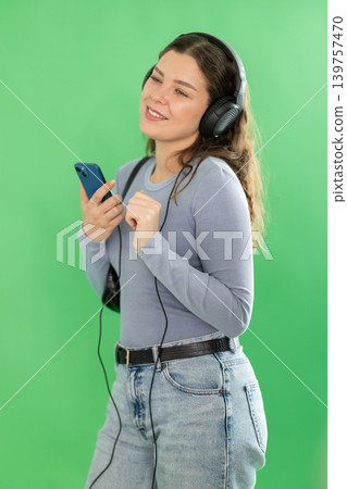 Young woman listening to music with headphones in front of green screen Young woman listening to music with headphones in front of green screen 139757470