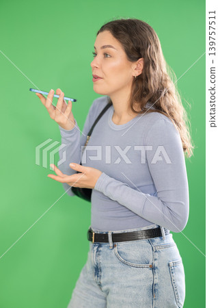 Young woman recording voice message in front of green screen Young woman recording voice message in front of green screen 139757511
