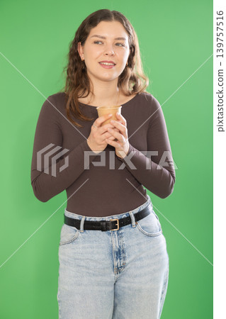 Young woman scrolling smartphone and drinking coffee in front of green screen Young woman scrolling smartphone and drinking coffee in front of green screen 139757516
