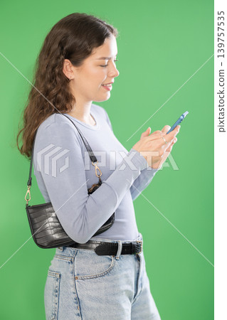 Young woman scrolling smartphone screen in front of green screen 139757535