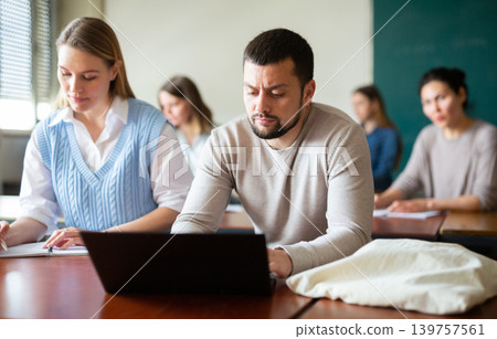 Handsome male student typing on laptop during lecture at university Handsome male student typing on laptop during lecture at university 139757561