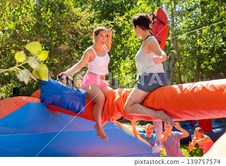 Happy girl funny pillow fighting on inflatable log with female friend 139757574