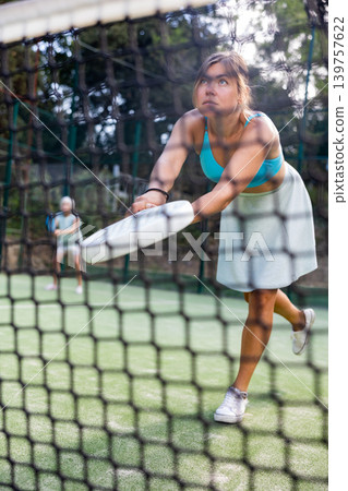View through net of young female paddle tennis player hitting ball View through net of young female paddle tennis player hitting ball 139757622