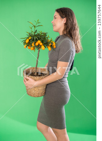 Young woman holding kumquat plant in pot in front of green screen Young woman holding kumquat plant in pot in front of green screen 139757644