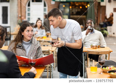 On open area of cafe, guy waiter communicates with girl customer, accepts order On open area of cafe, guy waiter communicates with girl customer, accepts order 139757705