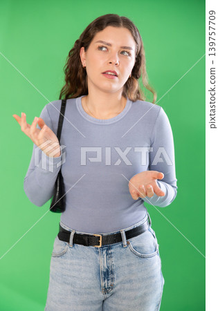 Thoughtful girl expresses bewilderment or forgetfulness on green background 139757709