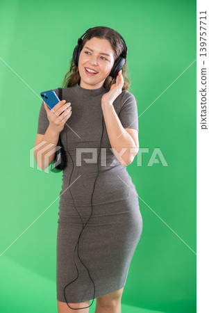 Young woman listening to music with headphones in front of green screen Young woman listening to music with headphones in front of green screen 139757711