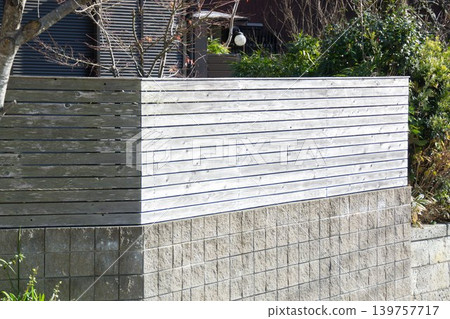 Exterior of a detached house with a wood-grain aluminum fence installed on top of concrete blocks. Exterior of a detached house with a wood-grain aluminum fence installed on top of concrete blocks. 139757717