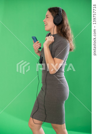 Young woman listening to music with headphones in front of green screen Young woman listening to music with headphones in front of green screen 139757718