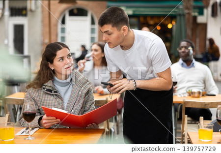 On open area of cafe, guy waiter communicates with girl customer, accepts order On open area of cafe, guy waiter communicates with girl customer, accepts order 139757729