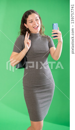 Csmiling pretty girl takes selfie on green background. Chroma key compositing. Csmiling pretty girl takes selfie on green background. Chroma key compositing. 139757741