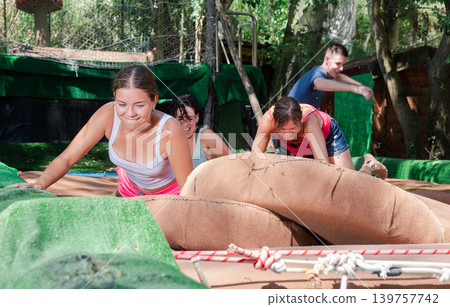 Playful girl moving through obstacle course over soft cushions in pool of water Playful girl moving through obstacle course over soft cushions in pool of water 139757742