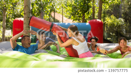 Cheerful girl fighting off friends with inflatable log while guarding toy chickens Cheerful girl fighting off friends with inflatable log while guarding toy chickens 139757775