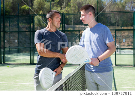 Adult and young men handshaking after padel tennis match 139757911