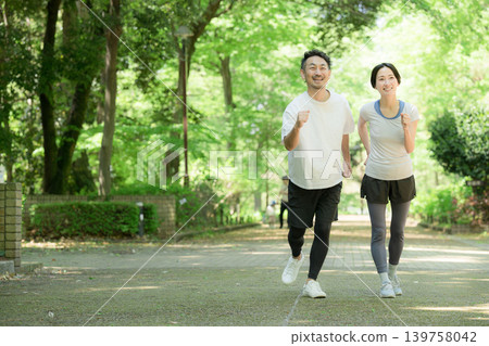 A healthy running couple enjoying jogging, running, and walking in a park surrounded by fresh greenery: a full-body exercise lifestyle. A healthy running couple enjoying jogging, running, and walking in a park surrounded by fresh greenery: a full-body exercise lifestyle. 139758042