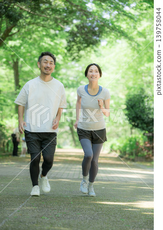 A healthy running couple enjoying jogging, running, and walking in a park surrounded by fresh greenery: a full-body exercise lifestyle. A healthy running couple enjoying jogging, running, and walking in a park surrounded by fresh greenery: a full-body exercise lifestyle. 139758044