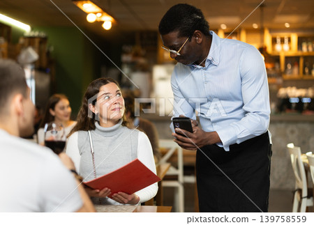 Woman, after reading the menu, makes an order from an African waiter Woman, after reading the menu, makes an order from an African waiter 139758559