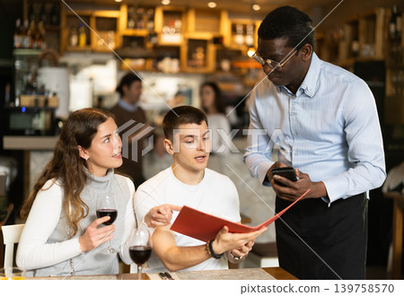African man listen to restaurant couple customer, writes down order African man listen to restaurant couple customer, writes down order 139758570