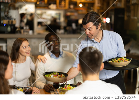 Man waiter serves cafe establishments couple visitor, puts food on table. Man waiter serves cafe establishments couple visitor, puts food on table. 139758574